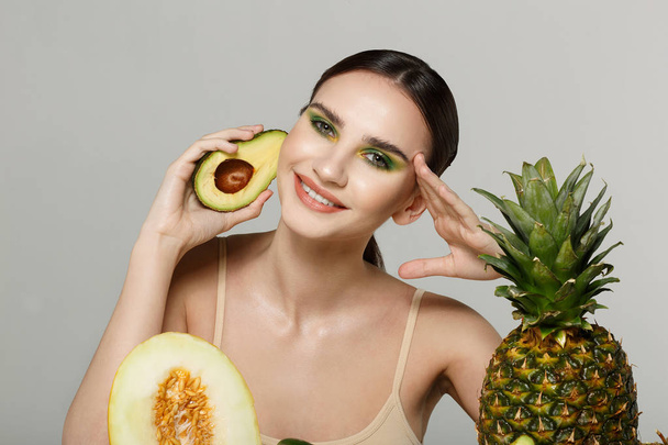 Gezonde mooie brunette meisje lacht, kijken naar de camera met avocado in de hand in de buurt van gezicht - Foto, afbeelding