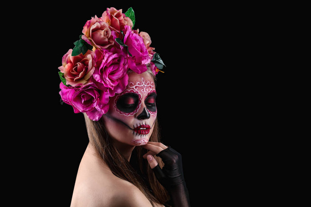 Jonge vrouw met geschilderde schedel op haar gezicht voor Mexico's dag van de doden tegen de donkere achtergrond - Foto, afbeelding