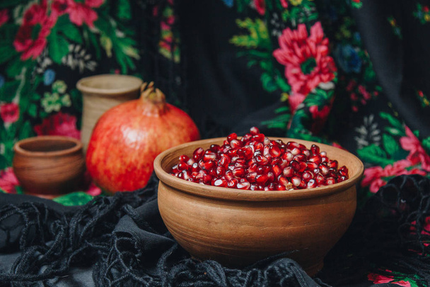 pomegranate grains in a ceramic bowl on a vintage fabric background, pomegranate fruit, ceramic jug, ceramic plate, ethnic shawl, Romma shawl, still life - Foto, imagen