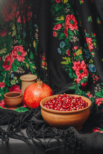 pomegranate grains in a ceramic bowl on a vintage fabric background, pomegranate fruit, ceramic jug, ceramic plate, ethnic shawl, Romma shawl, still life - Valokuva, kuva