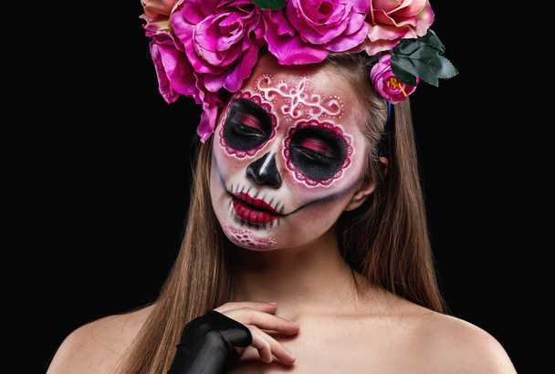 Jonge vrouw met geschilderde schedel op haar gezicht voor Mexico's dag van de doden tegen de donkere achtergrond - Foto, afbeelding