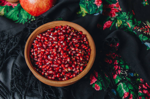 pomegranate grains in a ceramic bowl on a vintage fabric background, pomegranate fruit, ceramic jug, ceramic plate, ethnic shawl, Romma shawl, still life - Fotografie, Obrázek