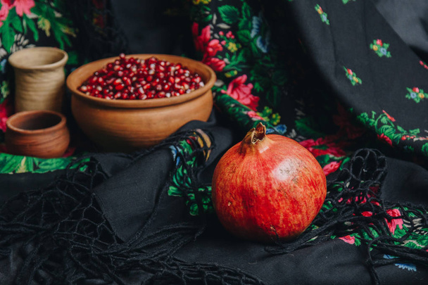 pomegranate grains in a ceramic bowl on a vintage fabric background, pomegranate fruit, ceramic jug, ceramic plate, ethnic shawl, Romma shawl, still life - Foto, afbeelding