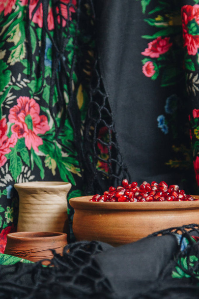 pomegranate grains in a ceramic bowl on a vintage fabric background, pomegranate fruit, ceramic jug, ceramic plate, ethnic shawl, Romma shawl, still life - Фото, изображение