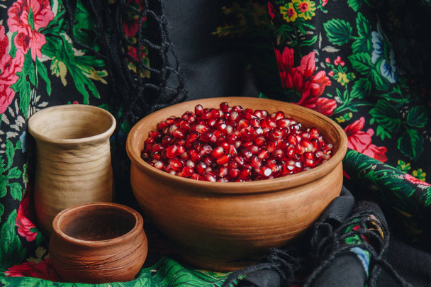 pomegranate grains in a ceramic bowl on a vintage fabric background, pomegranate fruit, ceramic jug, ceramic plate, ethnic shawl, Romma shawl, still life - Foto, Imagem