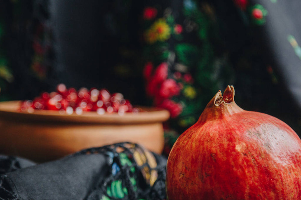 pomegranate grains in a ceramic bowl on a vintage fabric background, pomegranate fruit, ceramic jug, ceramic plate, ethnic shawl, Romma shawl, still life - Foto, afbeelding