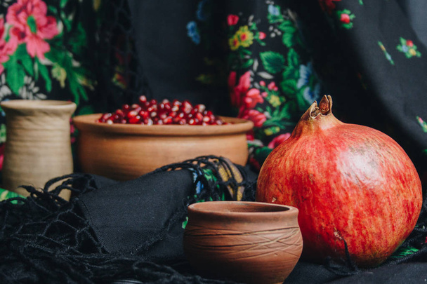 pomegranate grains in a ceramic bowl on a vintage fabric background, pomegranate fruit, ceramic jug, ceramic plate, ethnic shawl, Romma shawl, still life - Φωτογραφία, εικόνα