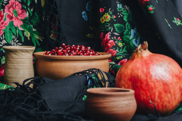 pomegranate grains in a ceramic bowl on a vintage fabric background, pomegranate fruit, ceramic jug, ceramic plate, ethnic shawl, Romma shawl, still life - Foto, imagen