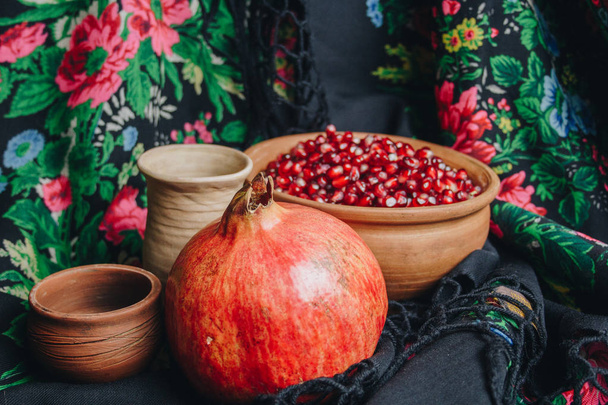 pomegranate grains in a ceramic bowl on a vintage fabric background, pomegranate fruit, ceramic jug, ceramic plate, ethnic shawl, Romma shawl, still life - Fotó, kép