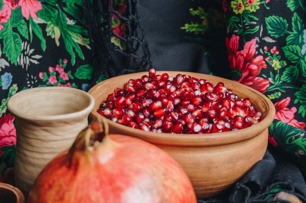 pomegranate grains in a ceramic bowl on a vintage fabric background, pomegranate fruit, ceramic jug, ceramic plate, ethnic shawl, Romma shawl, still life - Foto, Imagen