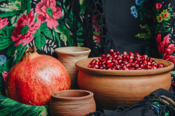 pomegranate grains in a ceramic bowl on a vintage fabric background, pomegranate fruit, ceramic jug, ceramic plate, ethnic shawl, Romma shawl, still life - Photo, Image