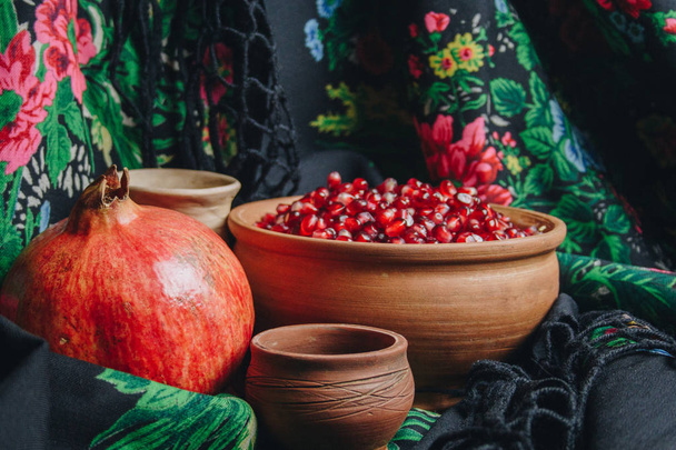 pomegranate grains in a ceramic bowl on a vintage fabric background, pomegranate fruit, ceramic jug, ceramic plate, ethnic shawl, Romma shawl, still life - 写真・画像