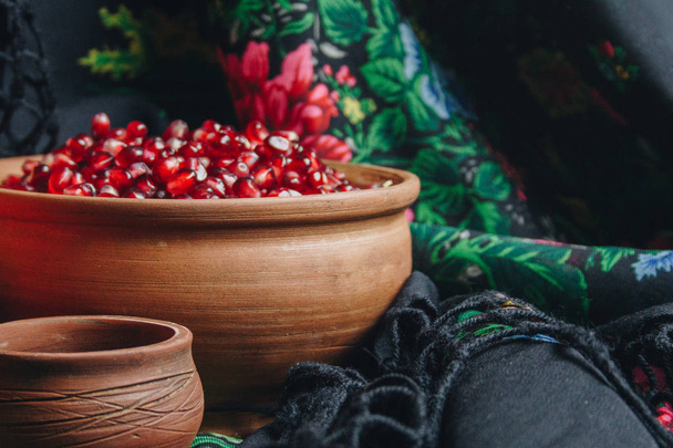 pomegranate grains in a ceramic bowl on a vintage fabric background, pomegranate fruit, ceramic jug, ceramic plate, ethnic shawl, Romma shawl, still life - Photo, Image