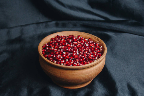 pomegranate grains in a ceramic bowl on a black fabric background, pomegranate fruit, ceramic jug, ceramic plate, isolated still life close up - Photo, image