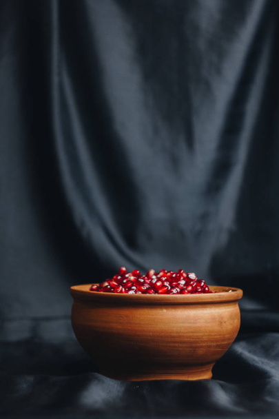 pomegranate grains in a ceramic bowl on a black fabric background, pomegranate fruit, ceramic jug, ceramic plate, isolated still life close up - Photo, Image