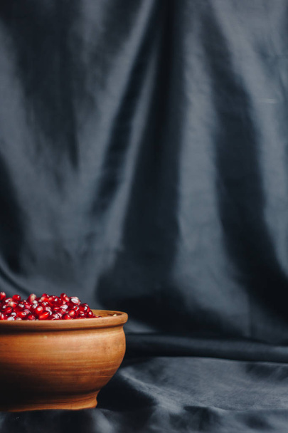 pomegranate grains in a ceramic bowl on a black fabric background, pomegranate fruit, ceramic jug, ceramic plate, isolated still life close up - Fotó, kép