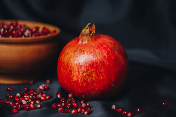 pomegranate grains in a ceramic bowl on a black fabric background, pomegranate fruit, ceramic jug, ceramic plate, isolated still life close up - Foto, afbeelding