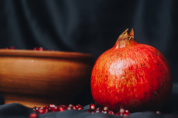 pomegranate grains in a ceramic bowl on a black fabric background, pomegranate fruit, ceramic jug, ceramic plate, isolated still life close up - Foto, immagini
