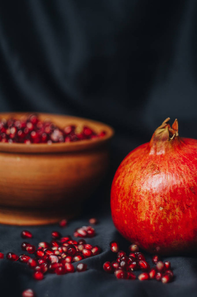 pomegranate grains in a ceramic bowl on a black fabric background, pomegranate fruit, ceramic jug, ceramic plate, isolated still life close up - Фото, изображение