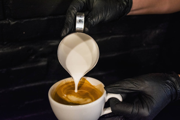 Process of preparation of a cappuccino with latte art. Work the barista in coffee shop. Black background and gloves. Fresh coffee - Photo, Image