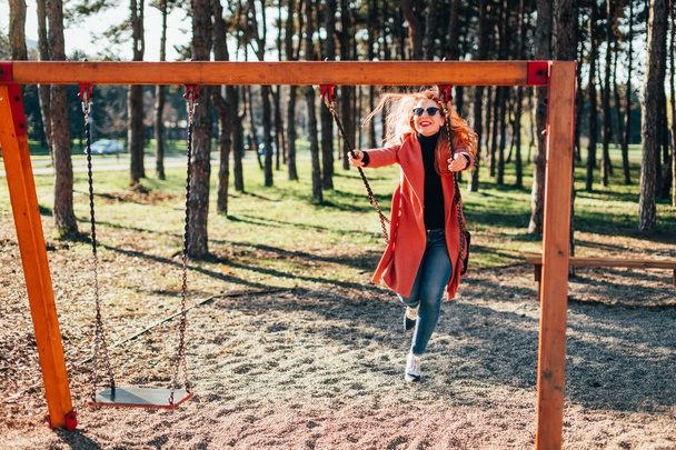 Young happy woman having fun on the swing in the playground - Photo, Image