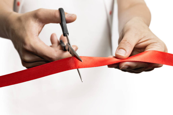The concept of the grand opening of something. Scissors in female hands cuts the red satin ribbon. - Photo, Image
