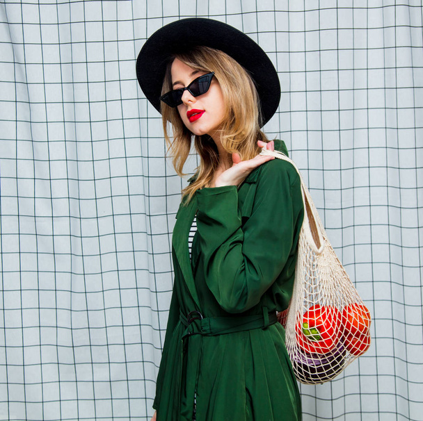 mulher de chapéu e capa verde no estilo dos anos 90 com saco de rede
 - Foto, Imagem