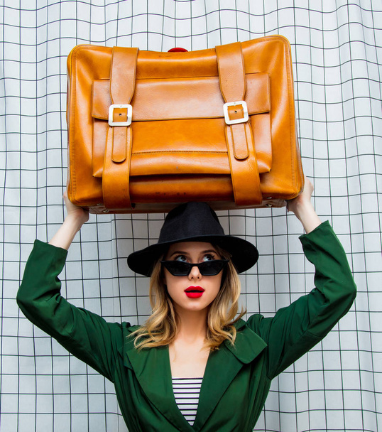 mujer en sombrero y capa verde en estilo 90 con maleta de viaje
  - Foto, imagen