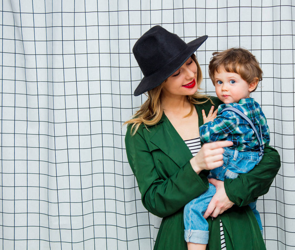 mulher de chapéu e capa verde no estilo dos anos 90 com menino criança
 - Foto, Imagem
