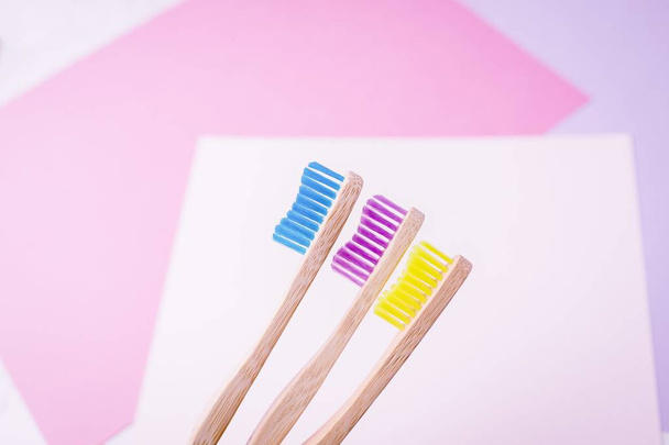 Cepillos de dientes de bambú amarillo, violeta y azul. Concepto ecológico. Fondo geométrico mínimo, de color. Copiar espacio
 - Foto, Imagen