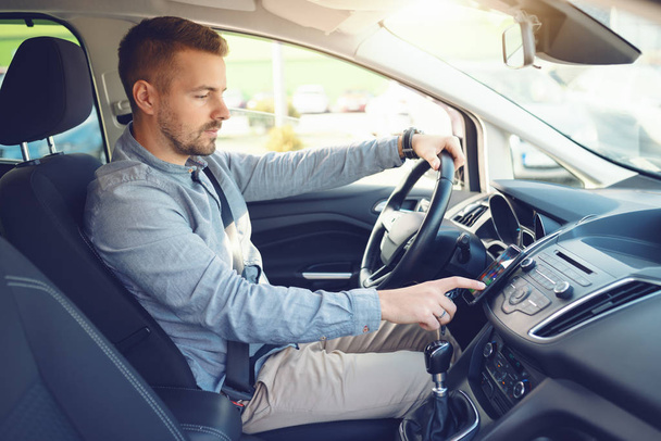 Caucásico hombre encendiendo la navegación en el teléfono inteligente mientras está sentado en su coche
. - Foto, imagen