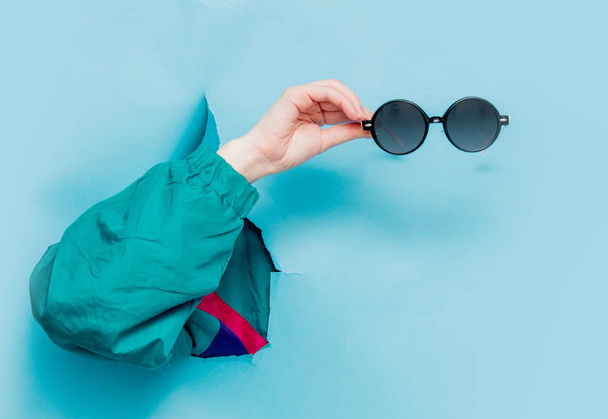Female hand in 90s style jacket holding suglasses  - 写真・画像