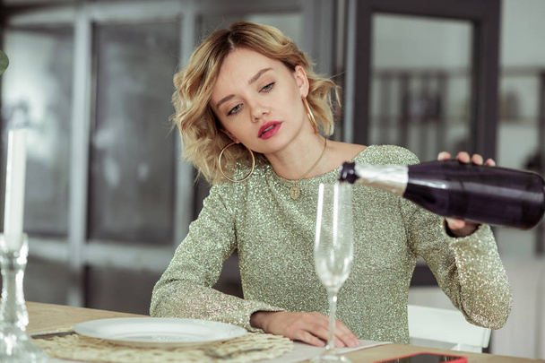 Blonde-haired curly woman pouring champagne into glass - Photo, Image