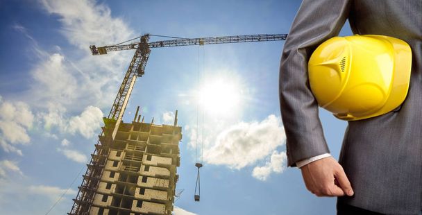 ingegnere in possesso di casco giallo per la sicurezza dei lavoratori sullo sfondo di nuova costruzione e costruzione gru
 - Foto, immagini