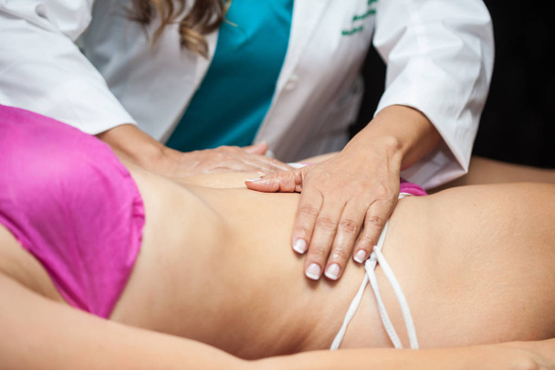 Arzt führt eine Bauchmassage an einer jungen Patientin durch - Foto, Bild