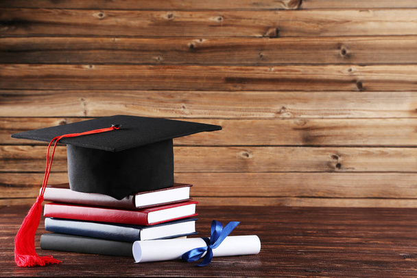 Graduation cap with diploma and stack of books on brown wooden t - Φωτογραφία, εικόνα