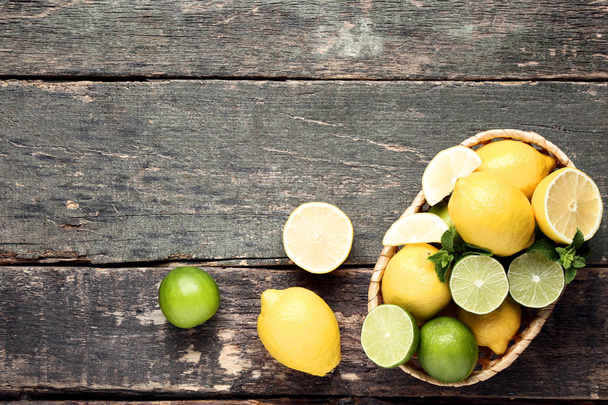 Lemons and limes with mint leafs in basket on wooden table - Foto, afbeelding