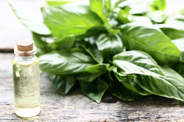 Bottle of essential oil with basil leafs on grey wooden table - Fotó, kép