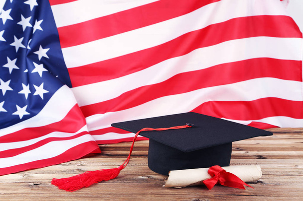Graduation cap with diploma and American flag on brown wooden ta - Foto, Imagen