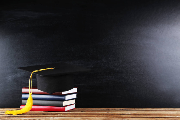 Graduation cap with stack of books on blackboard background - Foto, Imagem