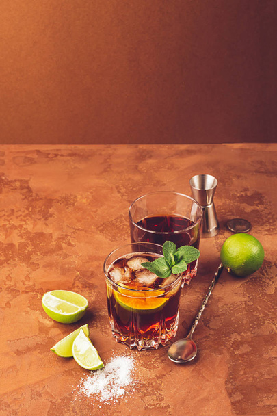 Коктейль из рома кубики льда и мяты в двух стаканах темно-коричневый фон. Алкогольный или безалкогольный махито
. - Фото, изображение