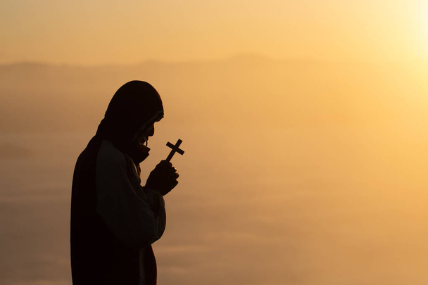 Silhouette of christian young man praying with a  cross at sunri - Photo, Image
