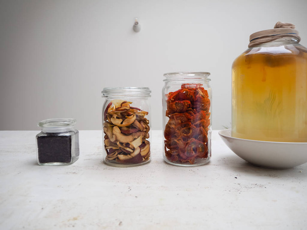 Черные чайные листья и сушеные ингредиенты, такие как яблоко рядом с большой банкой комбухи
 - Фото, изображение