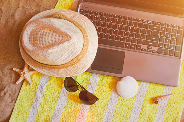 Kapelusz, laptop i okulary na ręcznik na piaszczystej plaży. - Zdjęcie, obraz