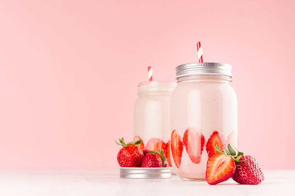 Strawberry smoothie in retro glass jar with bright sliced berries, straw and silver lid on light, soft, pink background, copy space. - Фото, изображение