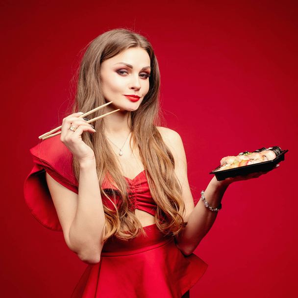 Woman in sexy red dress eating tasty sushi in studio - Фото, зображення