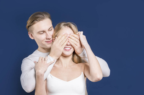 The guy covers his hands with the eyes of a girl. Happy young co - Foto, afbeelding