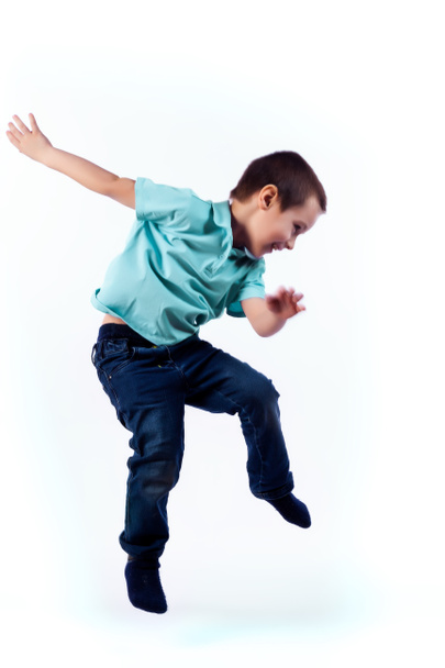 Glimlachend jongetje met donkere haren in spijkerbroek, blauwe polo t-shirt is springen en plezier op een afgelegen witte achtergrond in een fotostudio - Foto, afbeelding