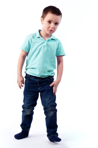 Little smiling boy with dark hair in blue jeans, blue polo t-shirt posing, laughing happily on a white isolated background in a photo studio. Portrait of happy joyful beautiful boy - Photo, Image