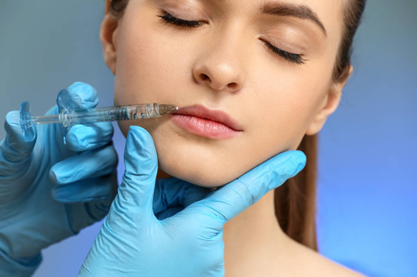 Young woman receiving injection in face on color background - Foto, Imagen
